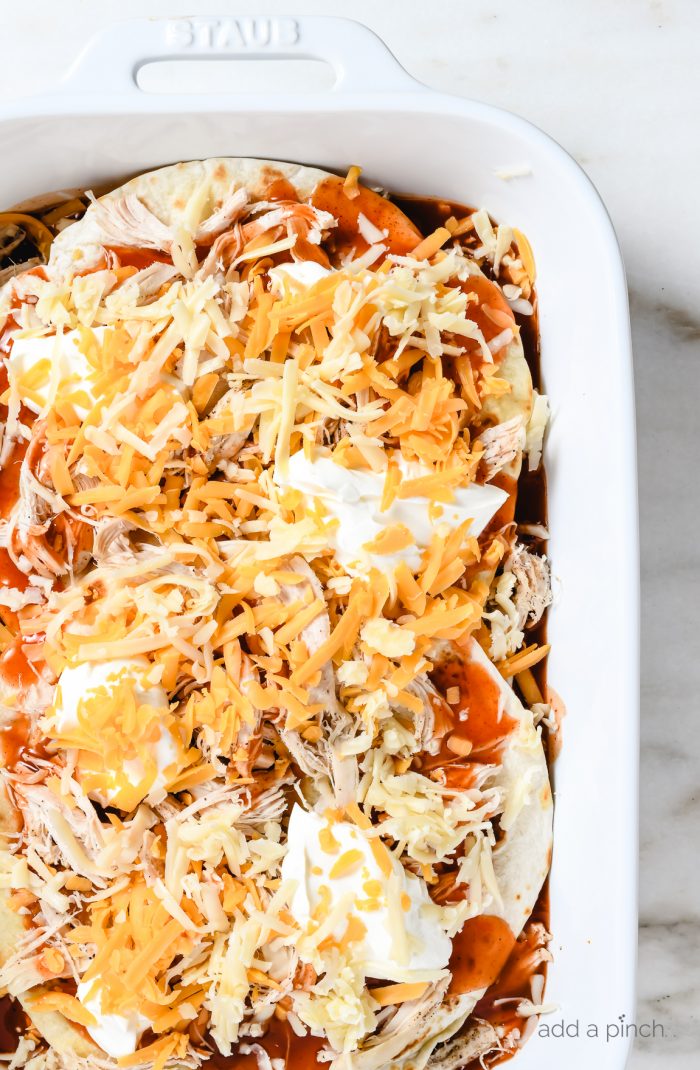 Two grated cheeses top chicken, tortillas, enchilada sauce and sour cream // addapinch.com