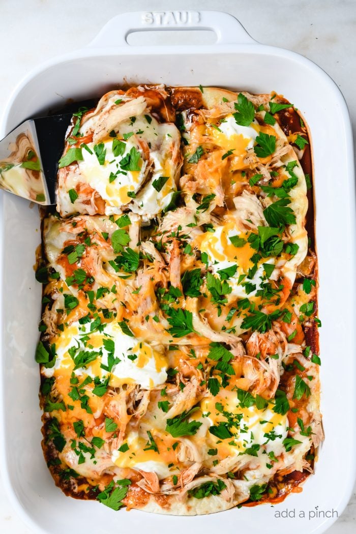 White baking dish with chicken enchilada casserole topped with fresh  cilantro and sour cream // addapinch.com