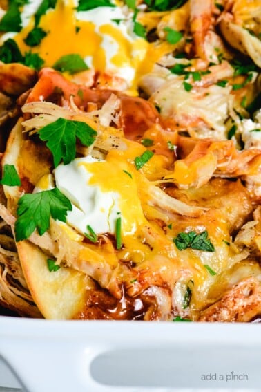 White baking dish holds layers of chicken, crispy tortillas, enchilada sauce, cheeses and more in this chicken enchilada casserole recipe.