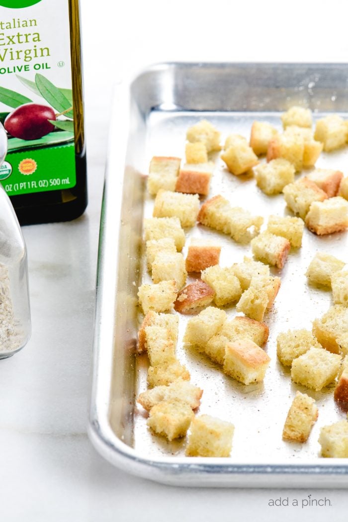 Ingredients for homemade croutons as well as rimmed baking sheet holding cut bread cubes // addapinch.com
