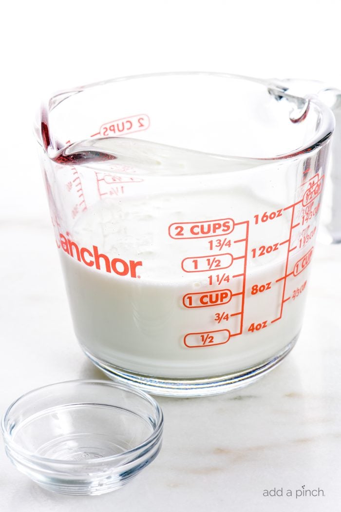 Glass measuring cup with milk and glass bowl with vinegar to make buttermilk substitute // addapinch.com