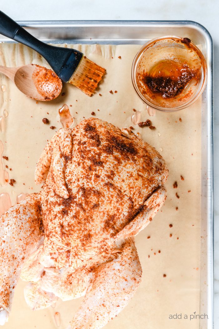 Photo of whole chicken coated with seasoning ready to be cooked for homemade easy rotisserie chicken.// addapinch.com