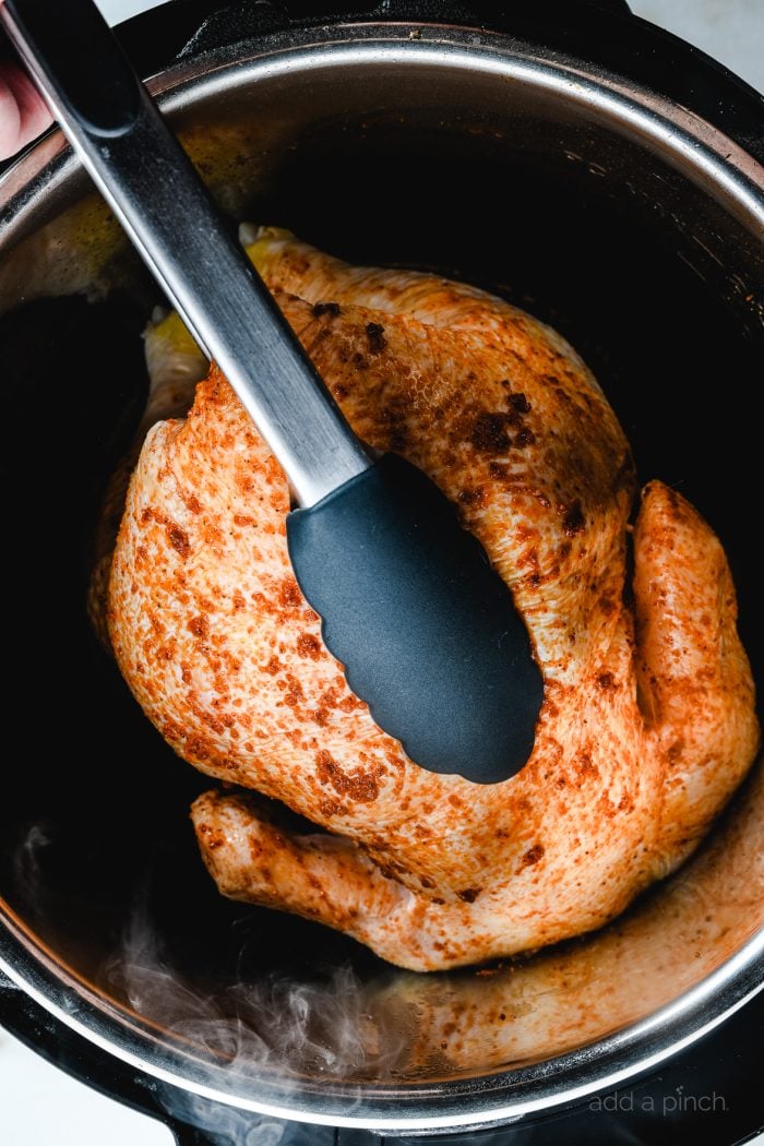 Photo of whole chicken in Instant Pot being turned with tongs. // addapinch.com