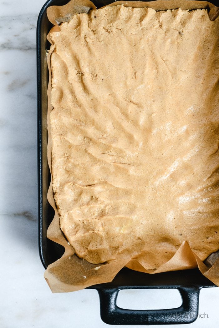Black baking dish with parchment paper and blondie crust pressed into the dish // addapinch.com