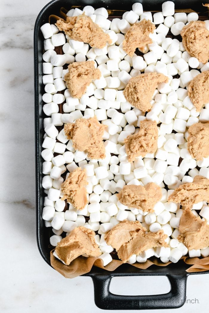 Baking dish lined in parchment with layer of mini marshmallows and dollops of blondie crust dough // addapinch.com