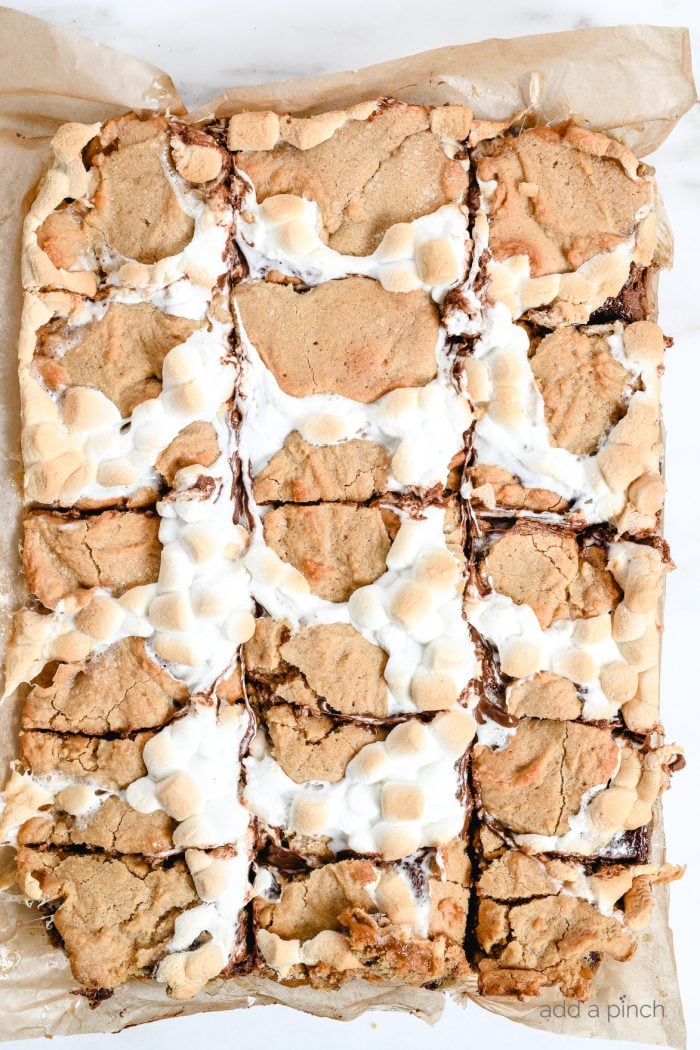 S'mores Bars showing melted chocolate, toasty marshmallows and blondie crust is cut into squares on a parchment paper // addapinch.com