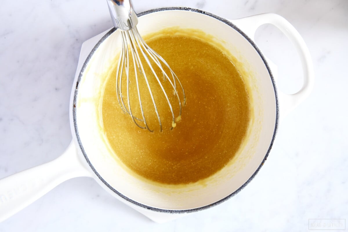 Whisking together caramel sauce in a white saucepan on a marble counter.