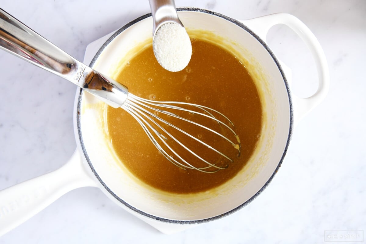 Adding salt to caramel sauce in a white saucepan on a marble counter.