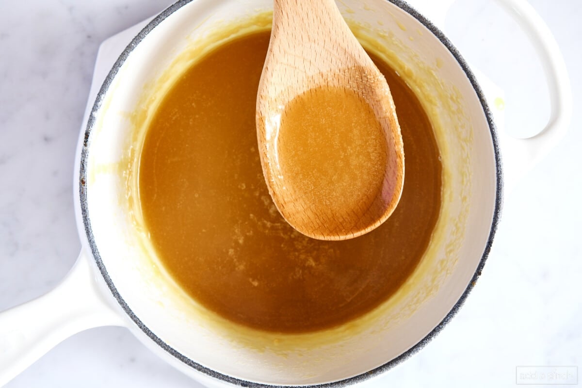 Caramel sauce with a wooden spoon in a white saucepan on a marble counter.