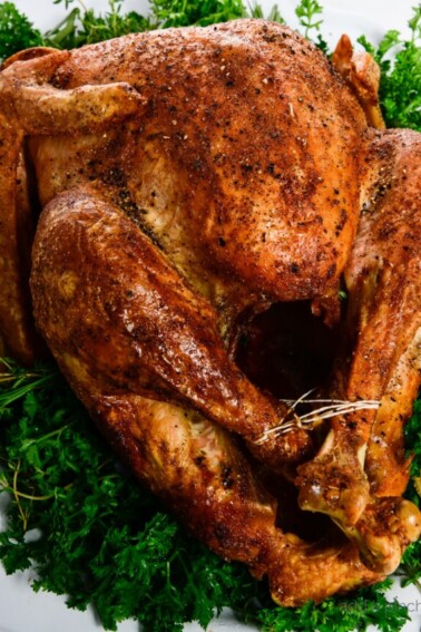 Photograph of golden brown roasted turkey served on a white platter with fresh herbs.