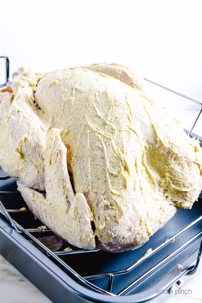 Side angle photograph of turkey on a roasting pan coated with seasoned butter ready to be roasted. // addapinch.com