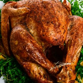 Photograph of golden brown roasted turkey served on a white platter with fresh herbs.