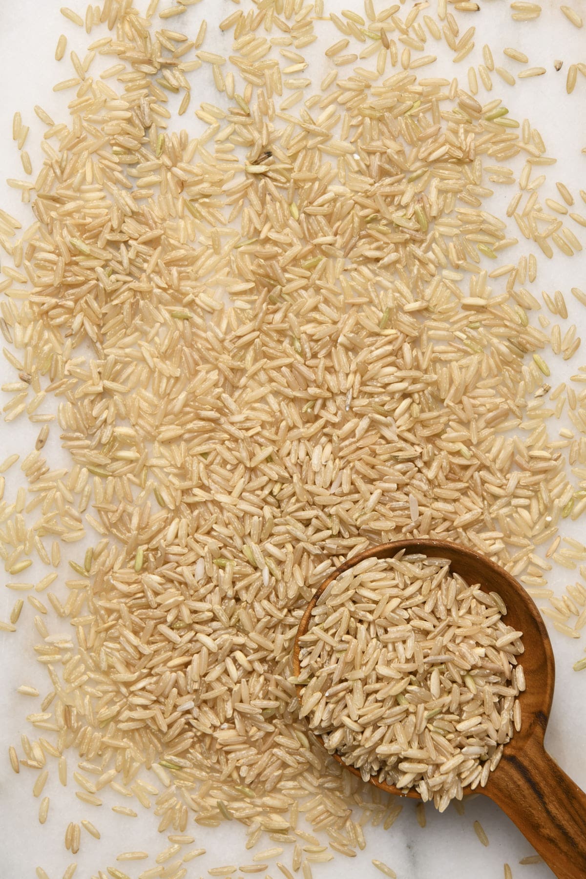 Photo of brown rice with a wooden scoop on a marble surface.