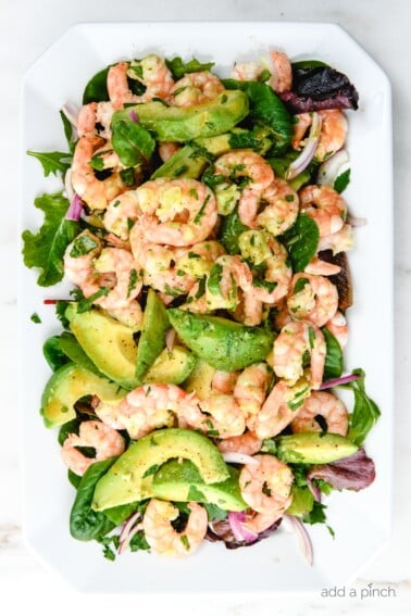 Photograph of citrus shrimp avocado salad on a white platter on white marble. // addapinch.com
