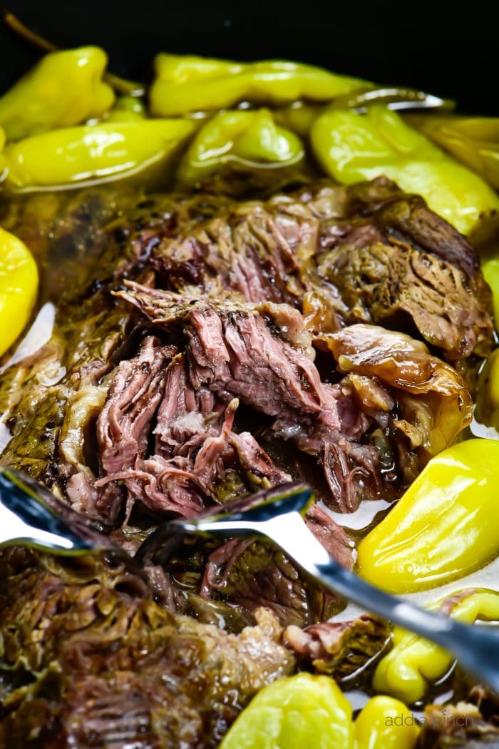 Photograph of slow cooked roast beef with pepperoncini peppers in a slow cooker. 