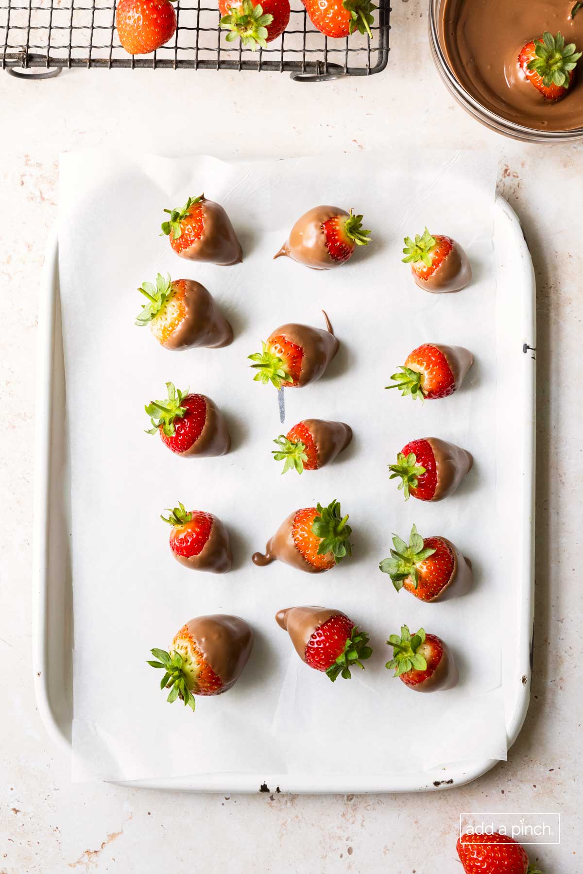 Platter lined with parchment paper and filled with strawberries dipped in chocolate drying.