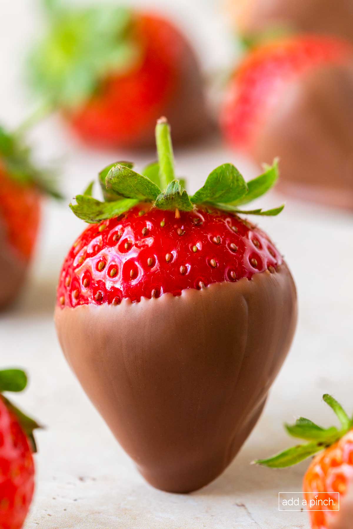 close photo of a single chocolate covered strawberry on a platter with other strawberries.