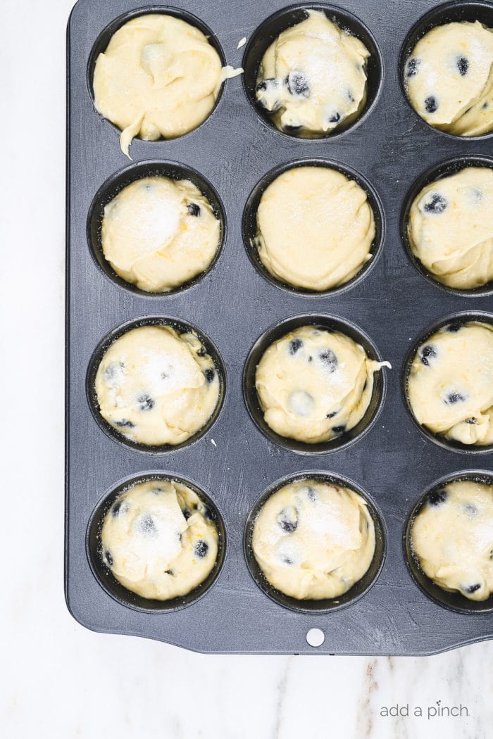 Muffin tin filled with muffin batter topped with sugar topping on a marble countertop.