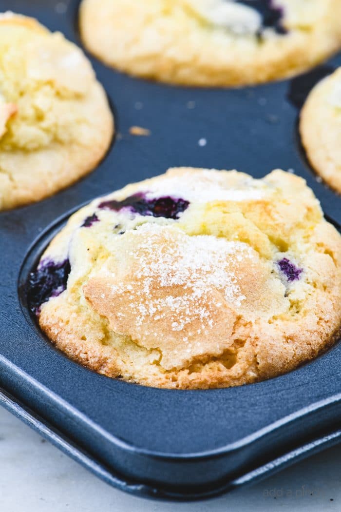 Baked muffins with sugar topping in a muffin tin set on a marble counter.