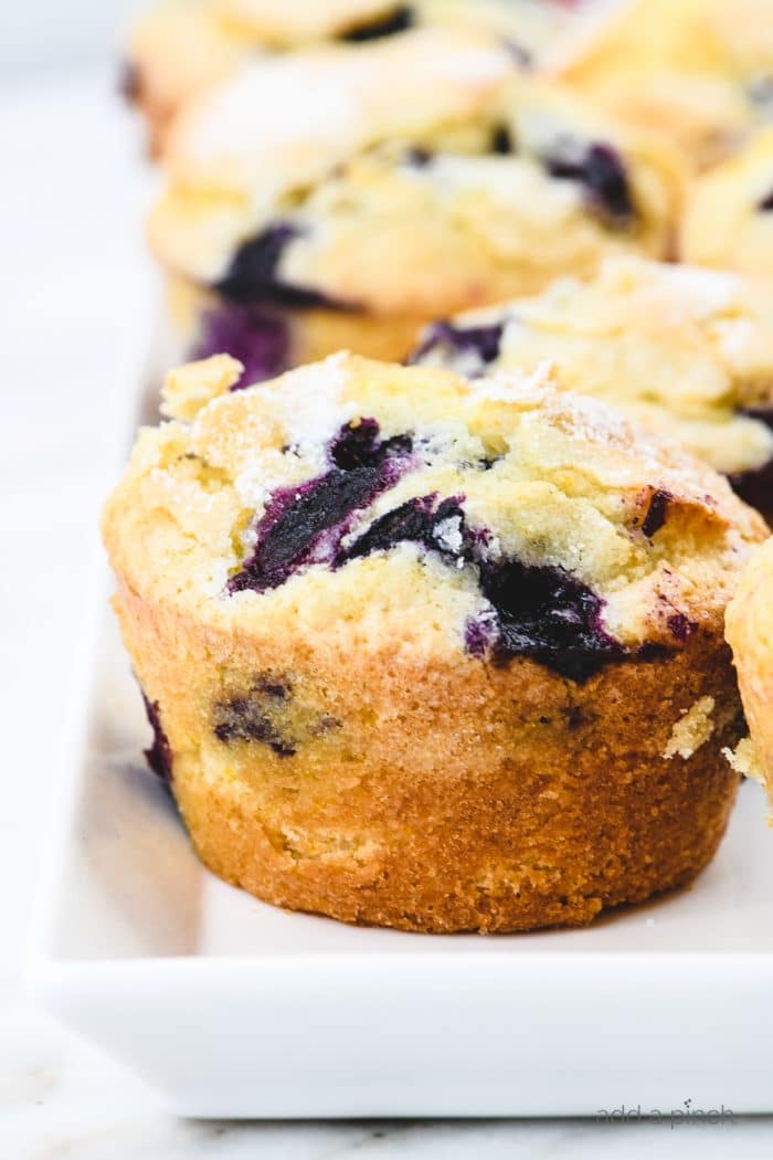 Baked homemade blueberry muffins on a white platter on a marble countertop.