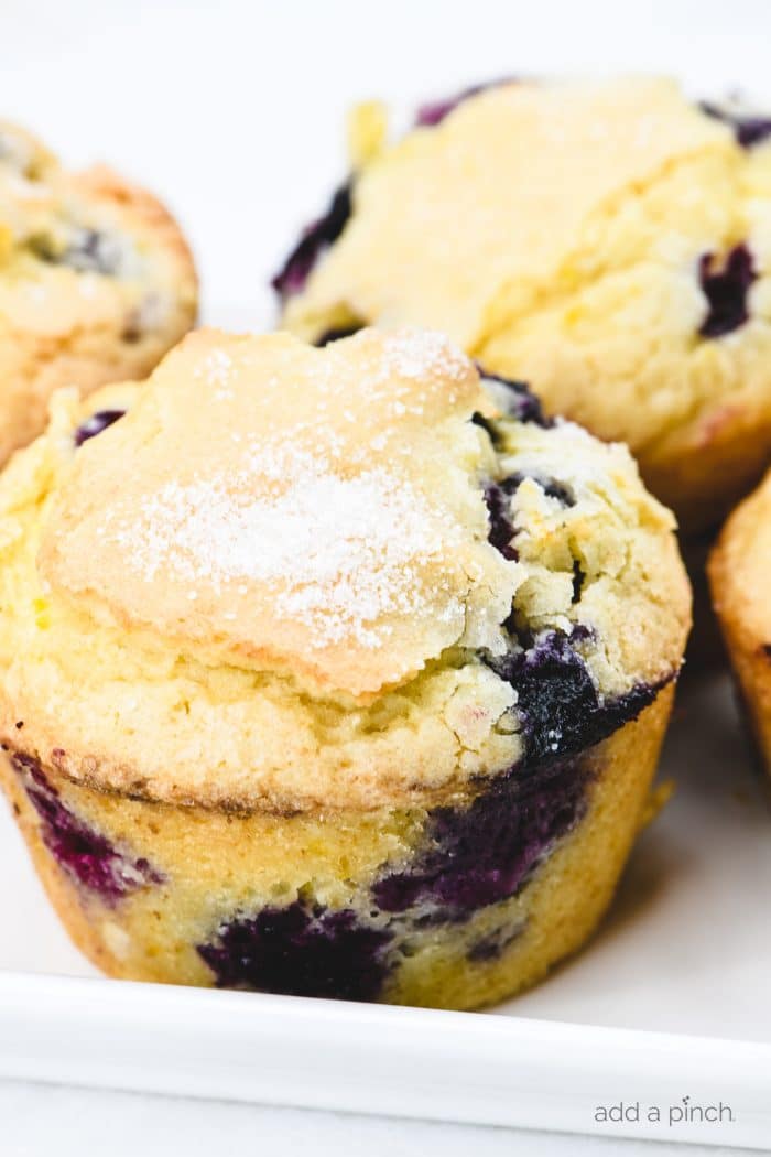 Close photograph of muffins filled with blueberries topped with sugar on a white platter.