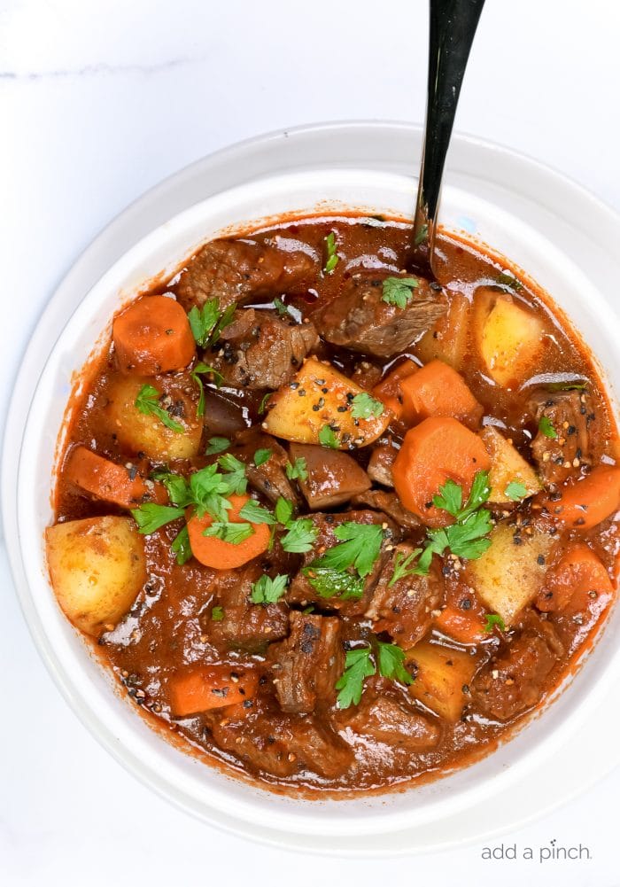 Photograph of beef stew in a white bowl on a white marble countertop. // addapinch.com