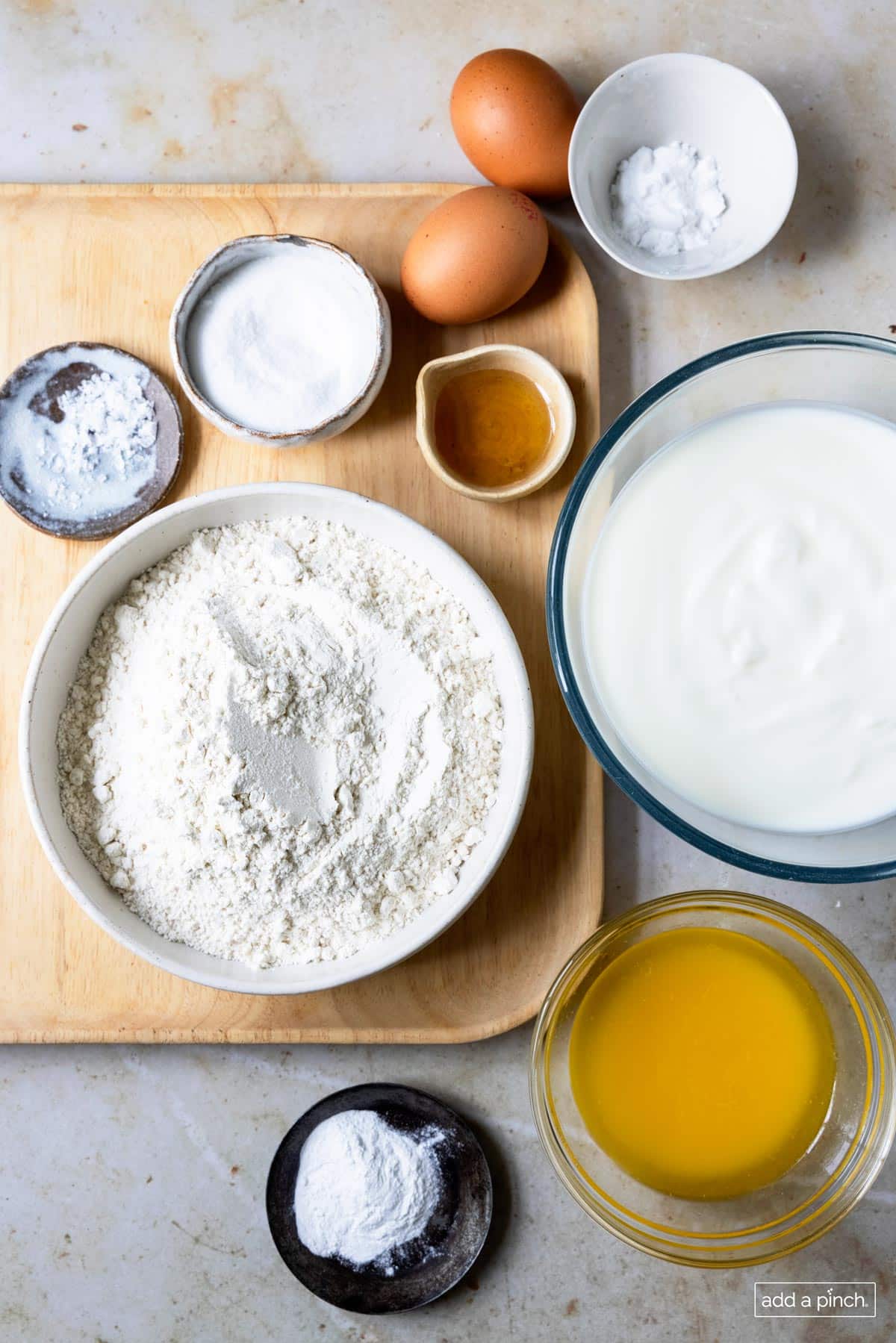 Photograph of all ingredients needed to make buttermilk pancakes in bowls on a wooden board and marble. 