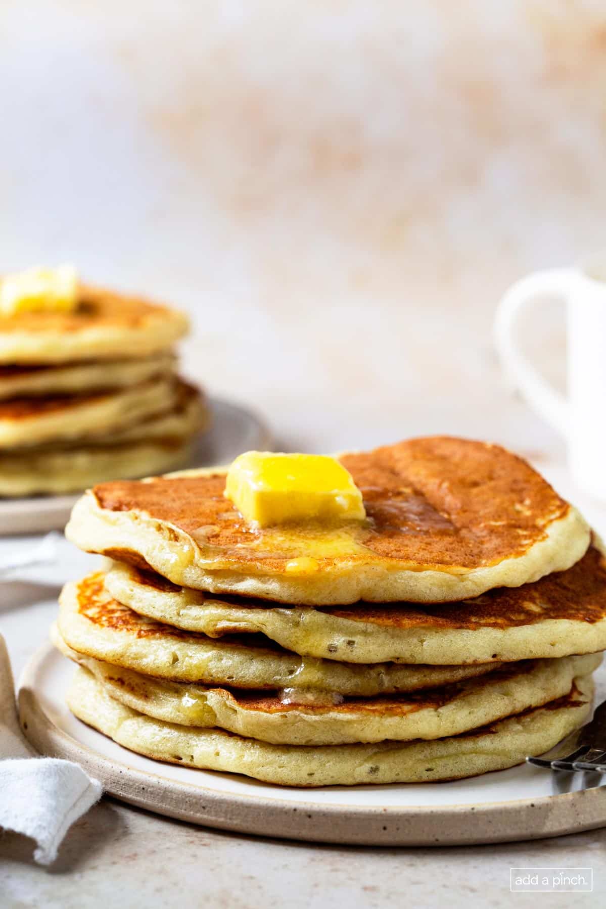 Image of stacks of pancakes on two plates topped with butter and syrup. 