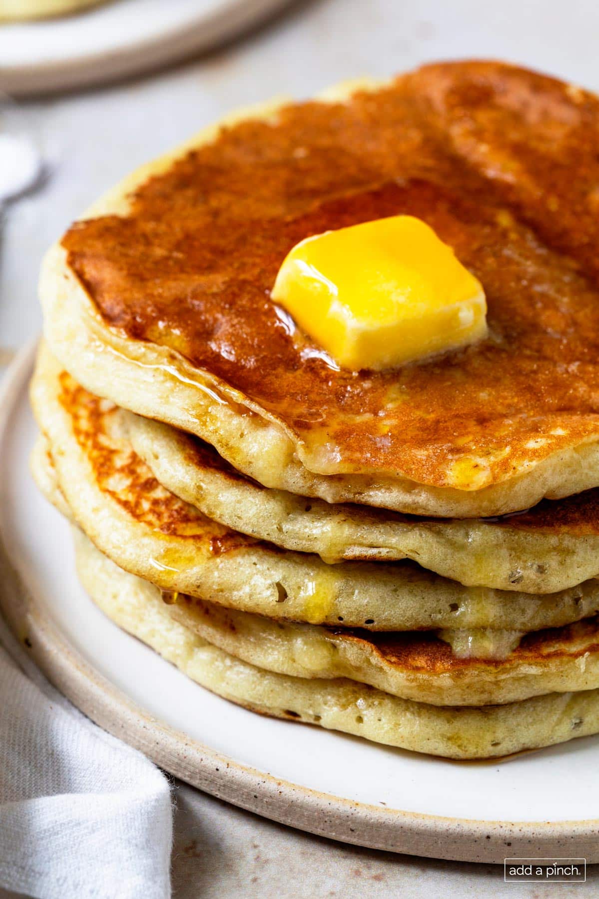 Photo of stack of pancakes topped with butter and syrup on a white plate.