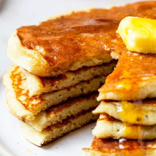 Photo of buttermilk pancakes topped with butter and syrup on a white plate.