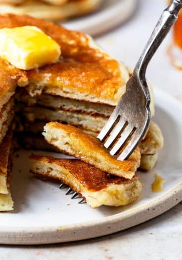Photograph of stack of buttermilk pancakes with a bite on a fork.