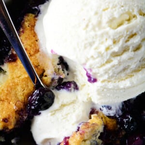 Photo of blueberry cobbler topped with vanilla ice cream in white bowl.