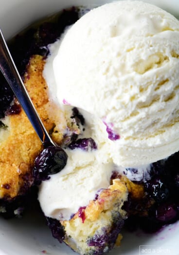 Photo of blueberry cobbler topped with vanilla ice cream in white bowl.
