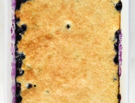 Baked golden cobbler topping on blueberries in a white baking dish.