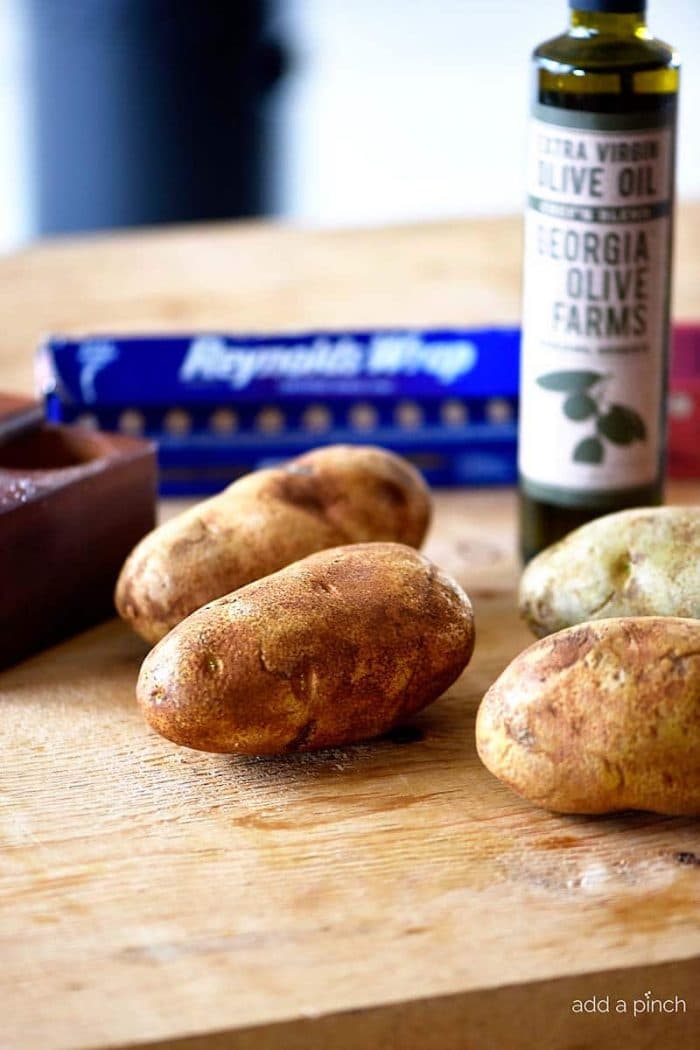 Photograph of russet potatoes, olive oil, salt and foil on a cutting board. // addapinch.com