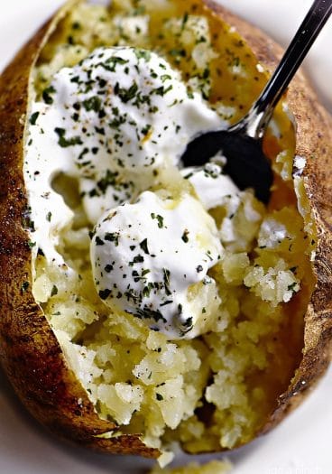 Overhead photograph of baked potato loaded with butter, sour cream and chives. // addapinch.com