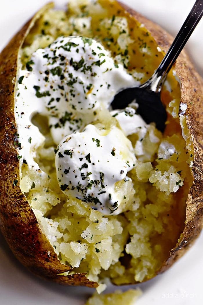 Overhead photograph of baked potato loaded with butter, sour cream and chives. // addapinch.com