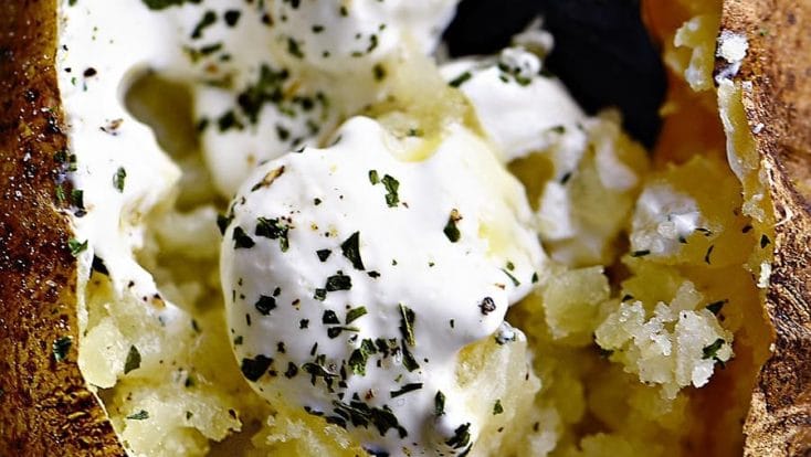 Overhead photograph of baked potato loaded with butter, sour cream and chives. // addapinch.com