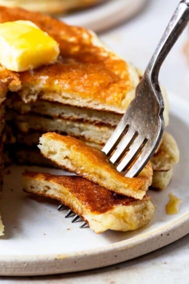Photograph of stack of buttermilk pancakes with a bite on a fork.