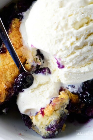 Photo of blueberry cobbler topped with vanilla ice cream in white bowl.