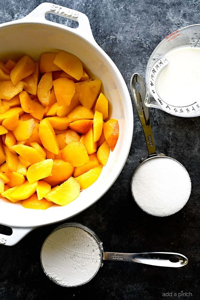 Sliced fresh juicy peaches in a white bowl with filled measuring cups on a stone countertop. 