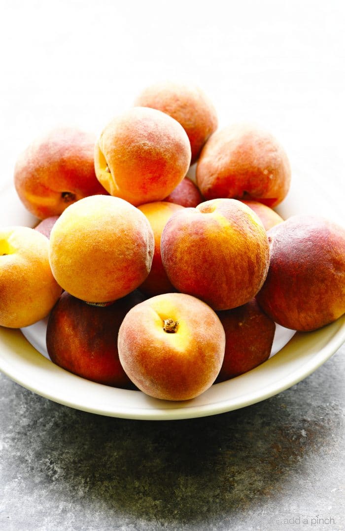 White bowl filled with fresh peaches on a stone countertop. 