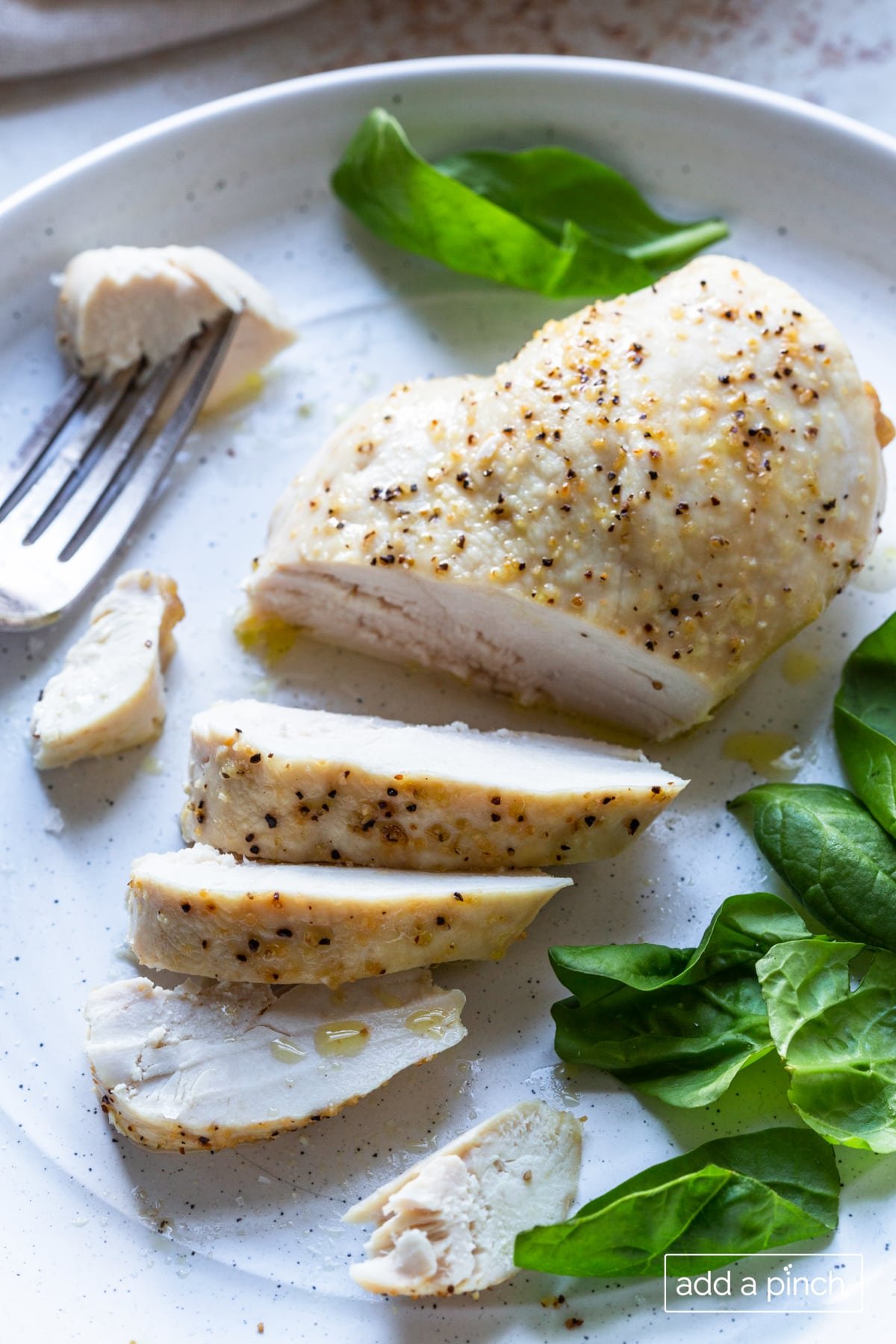 Photo of cooked chicken breast on a white plate with bite of chicken on a fork.