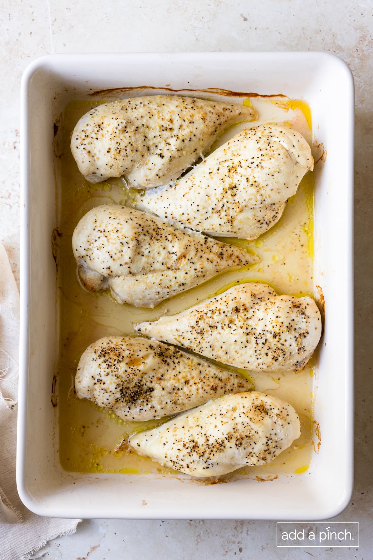 Photo of baked chicken breasts in a white baking dish on a white surface.