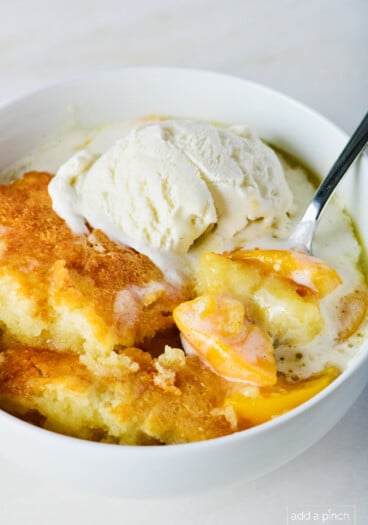 Photo of peach cobbler in a white bowl with vanilla ice cream