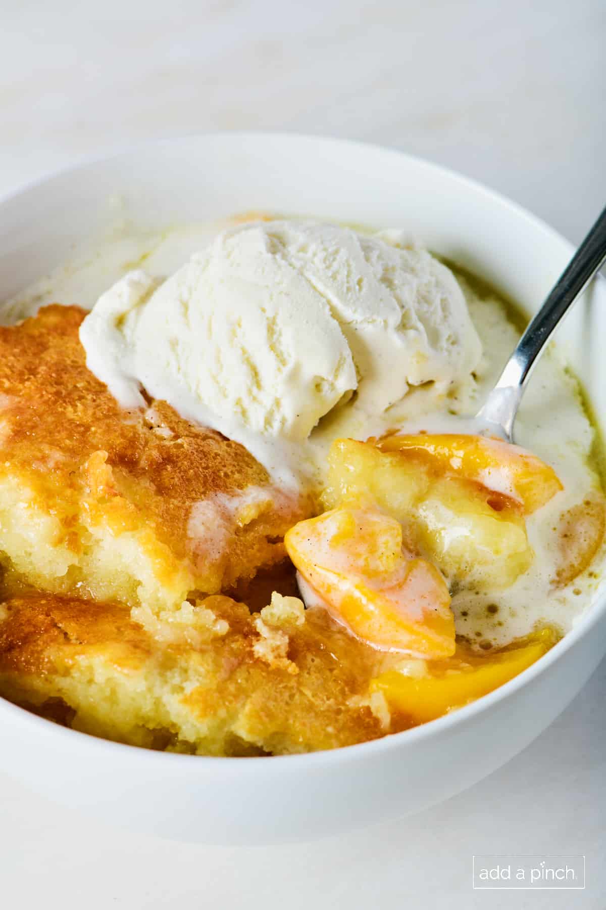 Photo of peach cobbler in a white bowl with vanilla ice cream