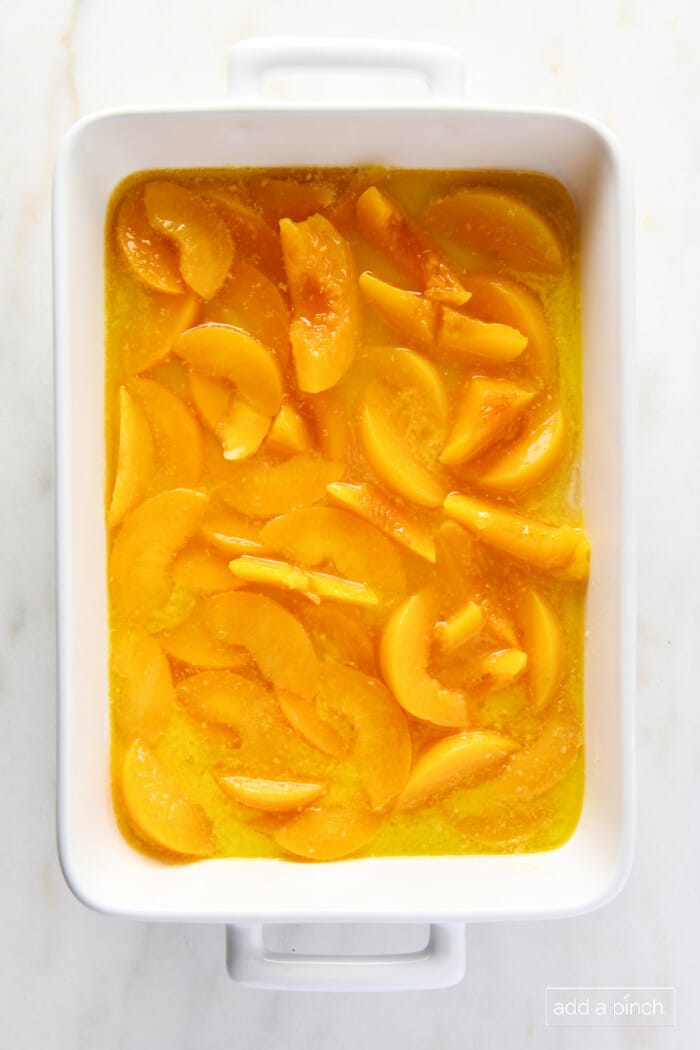 Peaches and butter in a white baking dish.