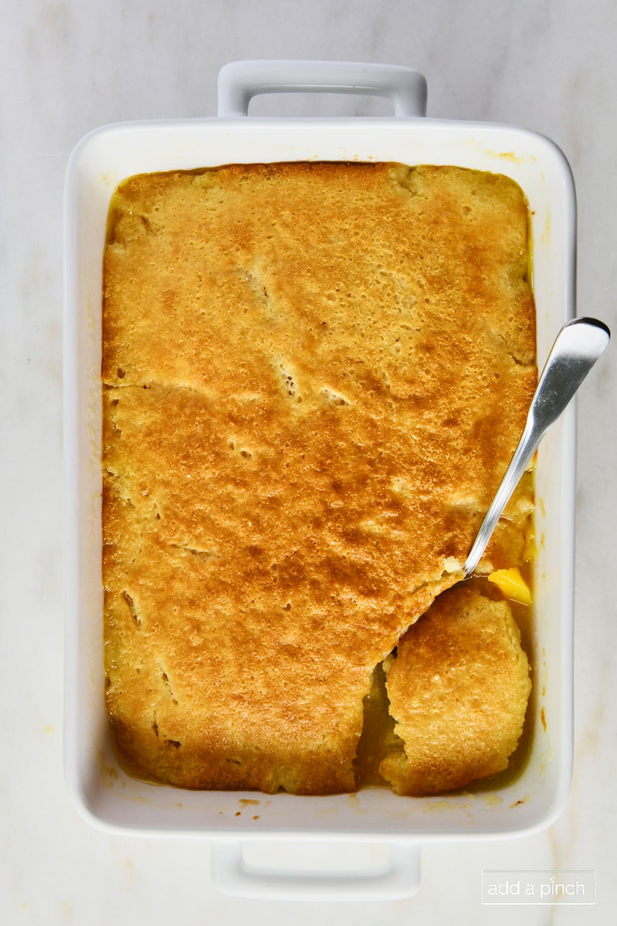 Baked peach cobbler in a white baking dish with a spoon