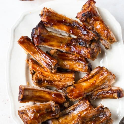Photo of BBQ ribs on a white platter on a white background.