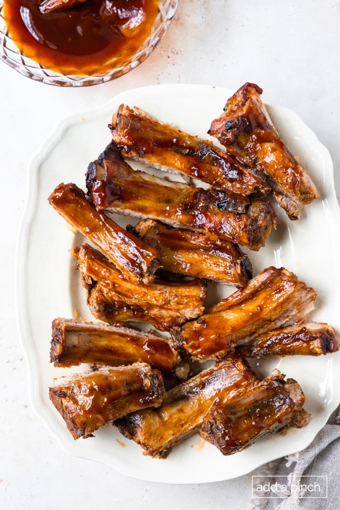 Photo of BBQ ribs on a white platter on a white background.